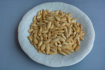Roasted Salty Pumpkin Seeds in a white plate on a blue background.