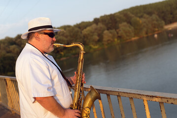 Man playing jazz on saxophone in the middle of the road on a sunny day in front of the bridge