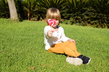 Portrait of a cute positive little boy with a heart shaped candy in green grass. Concept: mother's love, mother's day, Valentine's Day, first love, falling in love. Children summer mood, sweet life