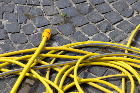A yellow watering hose lies on the cobblestones. Watering in the heat.	