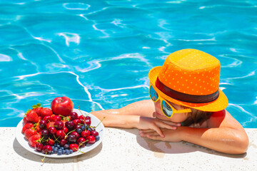 Happy child playing in swimming pool. Summer kids vacation. Summer fruit for children. Little kid boy relaxing in a pool having fun during summer vacation.