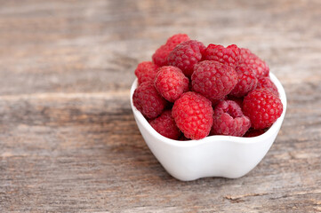 Seed ripe raspberries in a cup on a wooden background