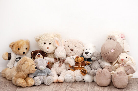 Many soft toys are sitting on the background of a white wall