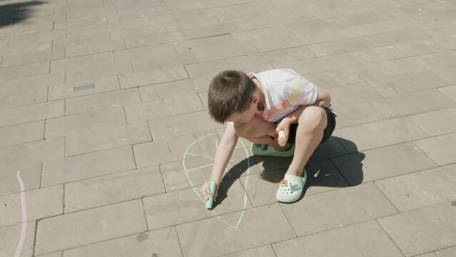 4K. A boy draws with colored crayons on the asphalt
