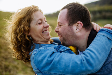 Outdoor portrait of mother hugging her grown up son with Down syndrome, motherhood concept.