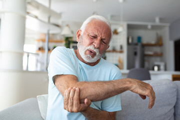 Senior man with arm pain.Old male massaging painful hand indoors. Old man hand holding his elbow...