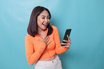 Fototapeta premium A portrait of a cheerful Asian woman looking at her smartphone over blue background