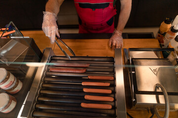Close-up of waiter standing by counter and prepairing hot-dog to a customer in cafe at gas station.