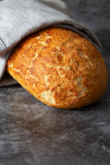 Tiger loaf of bread wrapped in a grey tea towel. On a black stone background