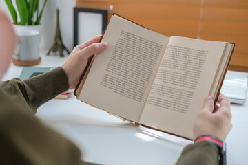Naklejka premium Over shoulder view, young man reading book in bright living room.