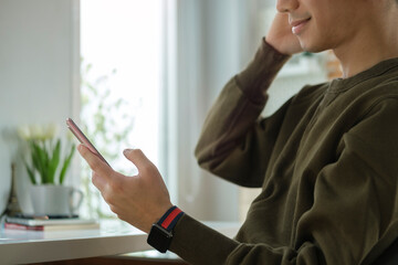 Cropped view of happy young asian man checking social media, texting message on mobile phone.