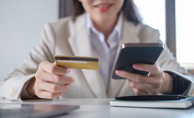 Smiling young woman holding credit card and smart phone for internet banking or shopping online.