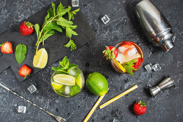 Fresh Mojito cocktail set with lime, mint, strawberry and ice in glass on stone background. Steel bar tools.