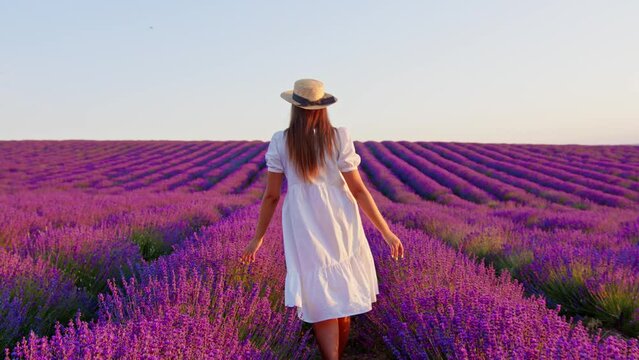 Young woman in white dress walking through a lavender field on sunset