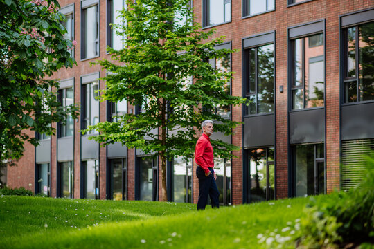 Businessman walking in park near office buliding during break, work life balance concept.