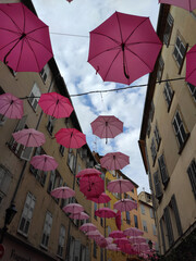 Suspended pink umbrellas in the historic center of Grasse, celebrating the Rose Expo in Provence-Alpes-Côte d'Azur, France. Elements of architecture of Grasse with colored umbrellas between houses.