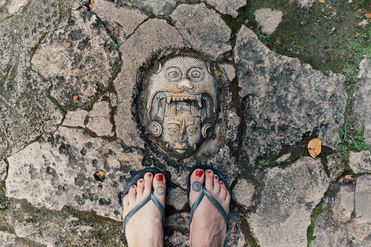 Mayan Fce Engraved In Stone On The Ground With Toes In Flip Flops