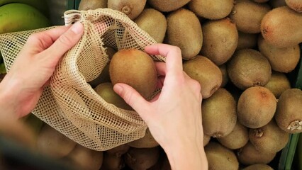 Woman picking kiwi fruits into reusable eco bag, sustainable shopping concept, over the shoulder shot. 