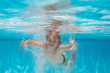 Underwater child in the swimming pool. Cute kid boy swimming in pool under water.