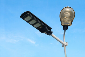 Solar LED lamp light with normal street light on pole against blue sky background.