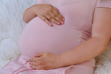 middle-aged pregnant woman in pink t-shirt holding her belly, waiting for newborn, concept of...