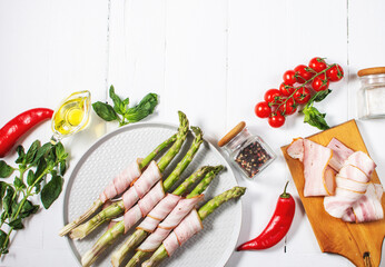 Fresh green asparagus wrapped in bacon on white wooden table. Top view