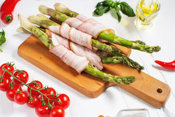 Fresh green asparagus wrapped in bacon on white wooden table