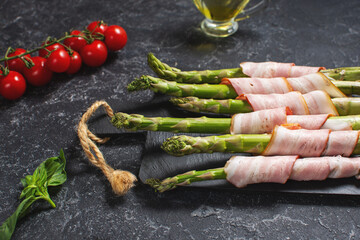 Fresh green asparagus wrapped in bacon on a stone table