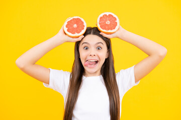 Funny face. Teenage girl holding a grapefruit on a yellow background.