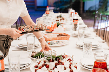waiter puts on the table a black tray with baked Japanese rolls.