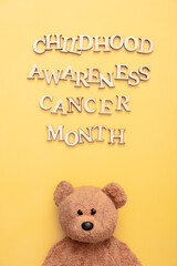 Childhood cancer awareness month text with teddy bear on yellow background. Vertical format