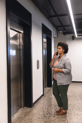 Mid adult biracial businesswoman talking on smartphone while waiting for elevator in office building © wavebreak3