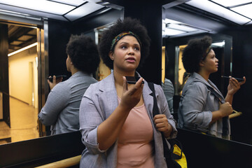 Mid adult biracial businesswoman talking on smartphone speaker while standing in elevator