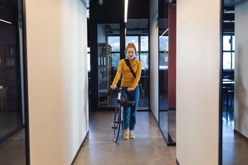 Mid adult caucasian businesswoman with bicycle in corridor of creative office