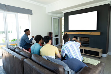 Obraz premium Multiracial male friends watching tv while relaxing on sofa in living room at home, copy space