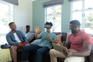 Cheerful multiracial friends looking at young man using virtual reality simulator gesturing at home