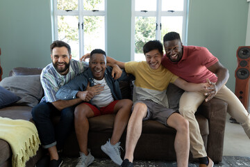 Obraz premium Portrait of carefree male multiracial friends laughing while resting on sofa in living room