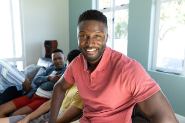 Portrait of smiling young man with multiracial male friends sitting on sofa in background at home