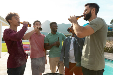 Carefree male multiracial friends having beer while chatting in barbecue party at yard, copy space