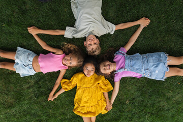 Happy friends lying in the grass, holding each other hands and having fun. Top view.