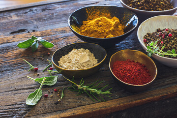 Verschiedene Gewürze und Kräuter auf einer rustikalen Holzplatte in bunten Schälchen bereitgestellt