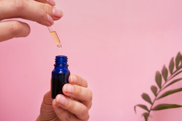 Cosmetic oil in dropper bottle in female hands. SPA and beauty therapy. Pink background with palm leaf decoration
