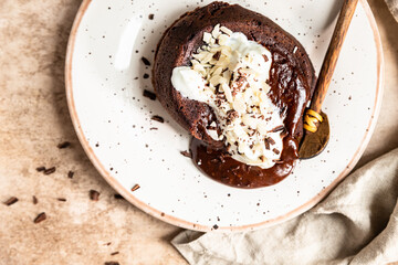 Chocolate fondant or lava cake with whipped cream, almond and chocolate pieces, brown background. Hot chocolate dessert or pudding with liquid center. Fondant au chocolate.