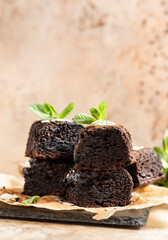 Stack of brownies made of dark chocolate served with cocoa and mint on baking paper, brown...