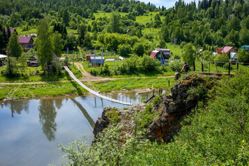 Suspension old wooden bridge over a small mountain river. Beautiful summer rural landscape with a bridge and green trees. 