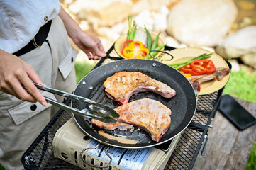 Female roasting a pork chop beef steak on a flying pan, cooking with a portable picnic stove
