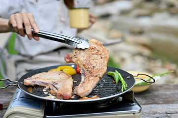 Female roasting a pork chop beef steak on a flying pan. cropped image. Outdoor camping.
