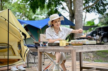 Female camper grill some pork-chop steaks on a portable outdoor picnic stove at campground.