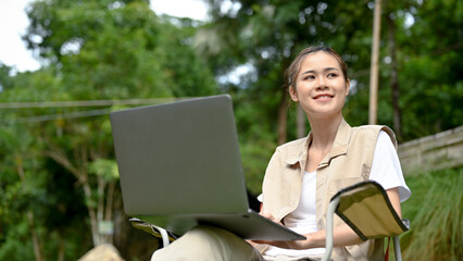 Beautiful young Asian female using laptop while looking at the beautiful view of nature forest.
