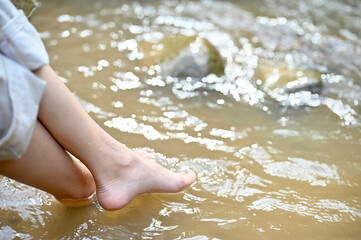A female relaxes sitting on the river stone, soaking her feet in the river. cropped image